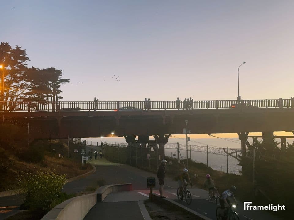 Cyclists riding under a bridge at sunset